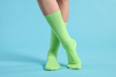 Photo of Woman in stylish lime socks on light blue background, closeup