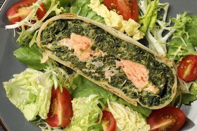 Photo of Piece of tasty strudel with salmon, spinach and salad on plate, top view