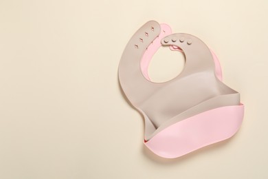 Photo of Color silicone baby bibs on beige background, top view. Space for text