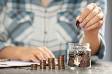 Photo of Woman putting money into glass jar at table, closeup