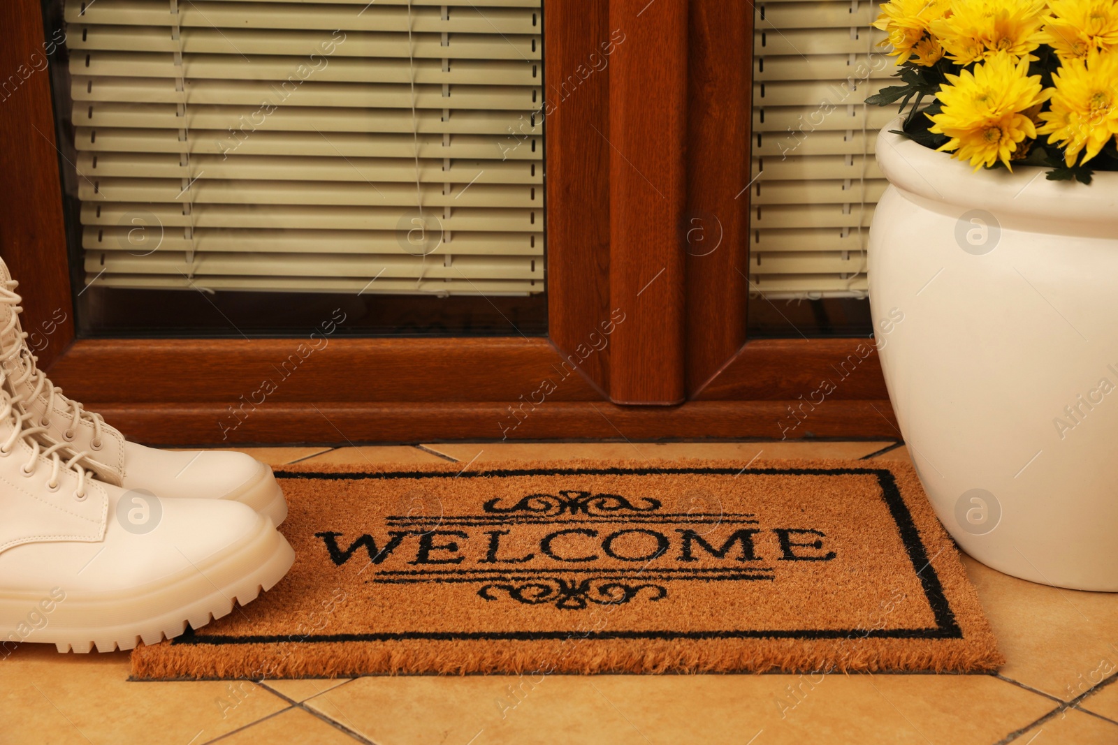 Photo of Door mat with word Welcome, stylish boots and beautiful flowers on floor near entrance