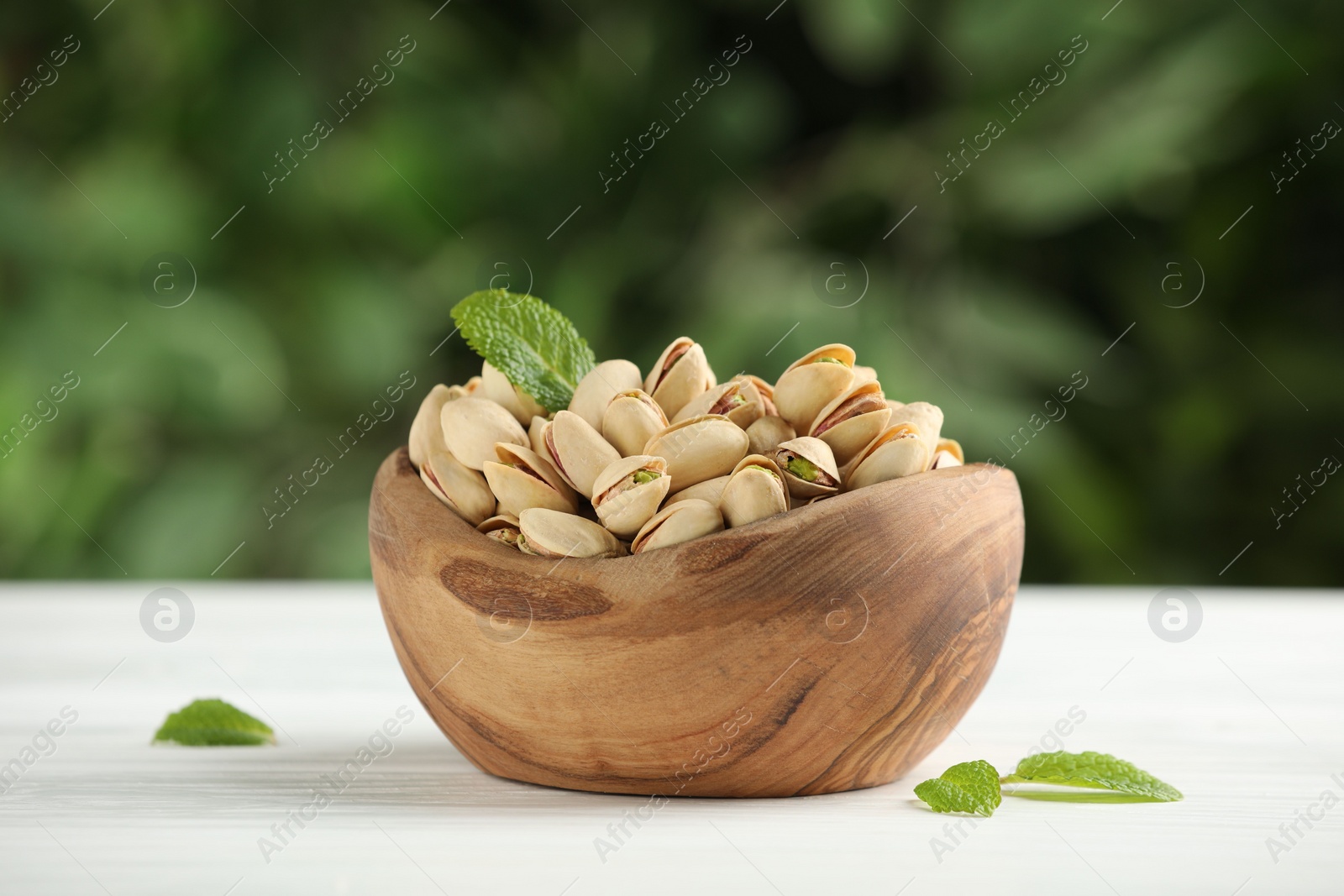 Photo of Tasty pistachios in bowl on white table against blurred background