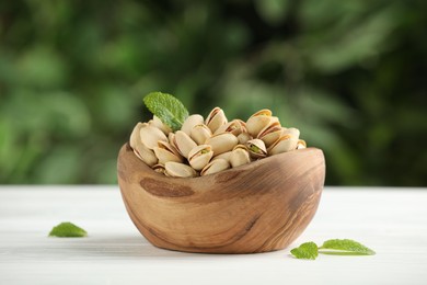 Photo of Tasty pistachios in bowl on white table against blurred background