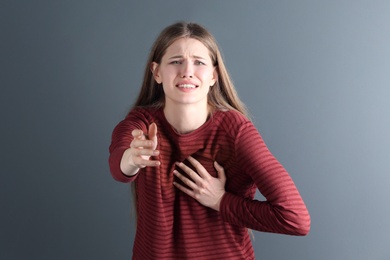 Young woman having heart attack on gray background