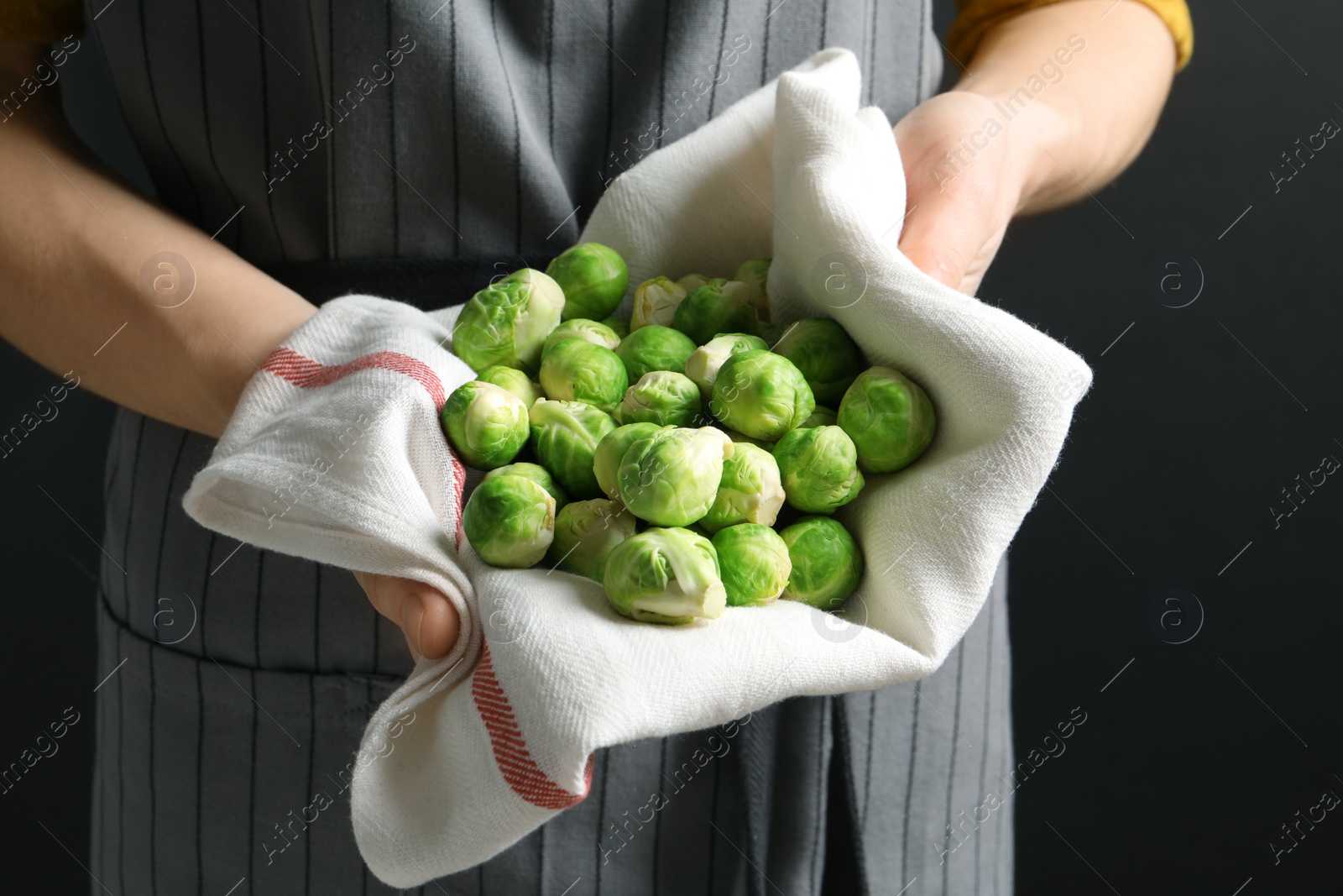 Photo of Woman holding heap of fresh Brussels sprouts in towel, closeup