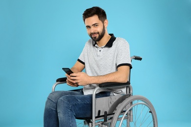 Young man with smartphone in wheelchair on color background