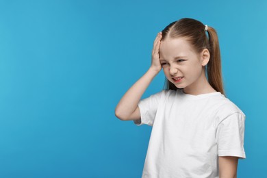 Little girl suffering from headache on light blue background. Space for text