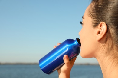 Photo of Young sporty woman drinking from water bottle outdoors on sunny day. Space for text