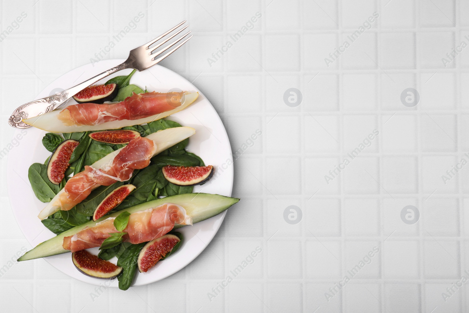 Photo of Tasty melon, jamon and figs on white tiled table, top view. Space for text