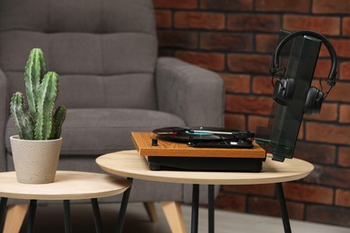Stylish turntable with vinyl record, headphones and houseplant on table indoors