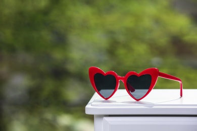 Photo of Stylish heart shaped sunglasses on table against blurred background. Space for text