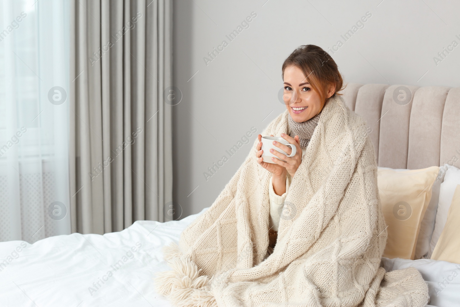 Photo of Happy beautiful woman with warm plaid and cup of drink in bed at home