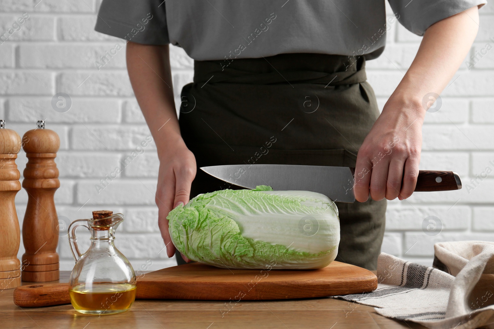 Photo of Woman cutting fresh Chinese cabbage at wooden table indoors, closeup