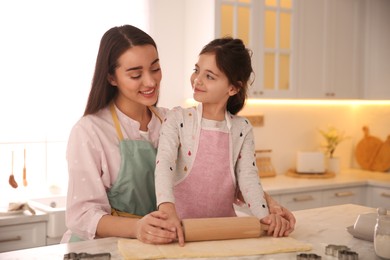 Mother with her cute little daughter rolling dough in kitchen