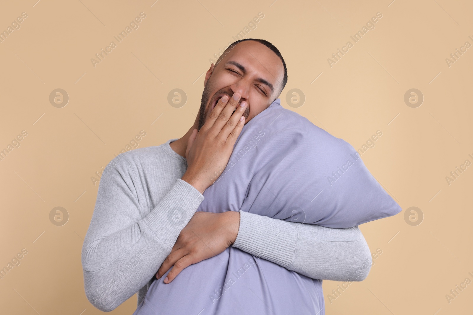 Photo of Sleepy man with pillow yawning on beige background. Insomnia problem