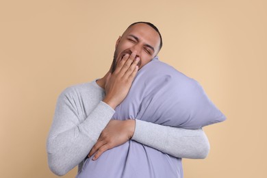 Sleepy man with pillow yawning on beige background. Insomnia problem