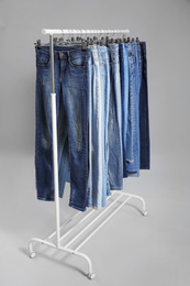 Photo of Rack with different jeans on grey background