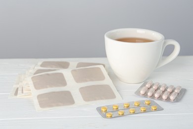 Photo of Mustard plasters, pills and cup of tea on white wooden table