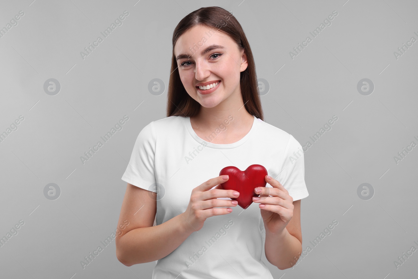 Photo of Smiling woman holding red heart on light grey background