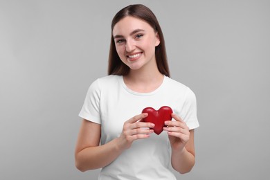 Photo of Smiling woman holding red heart on light grey background