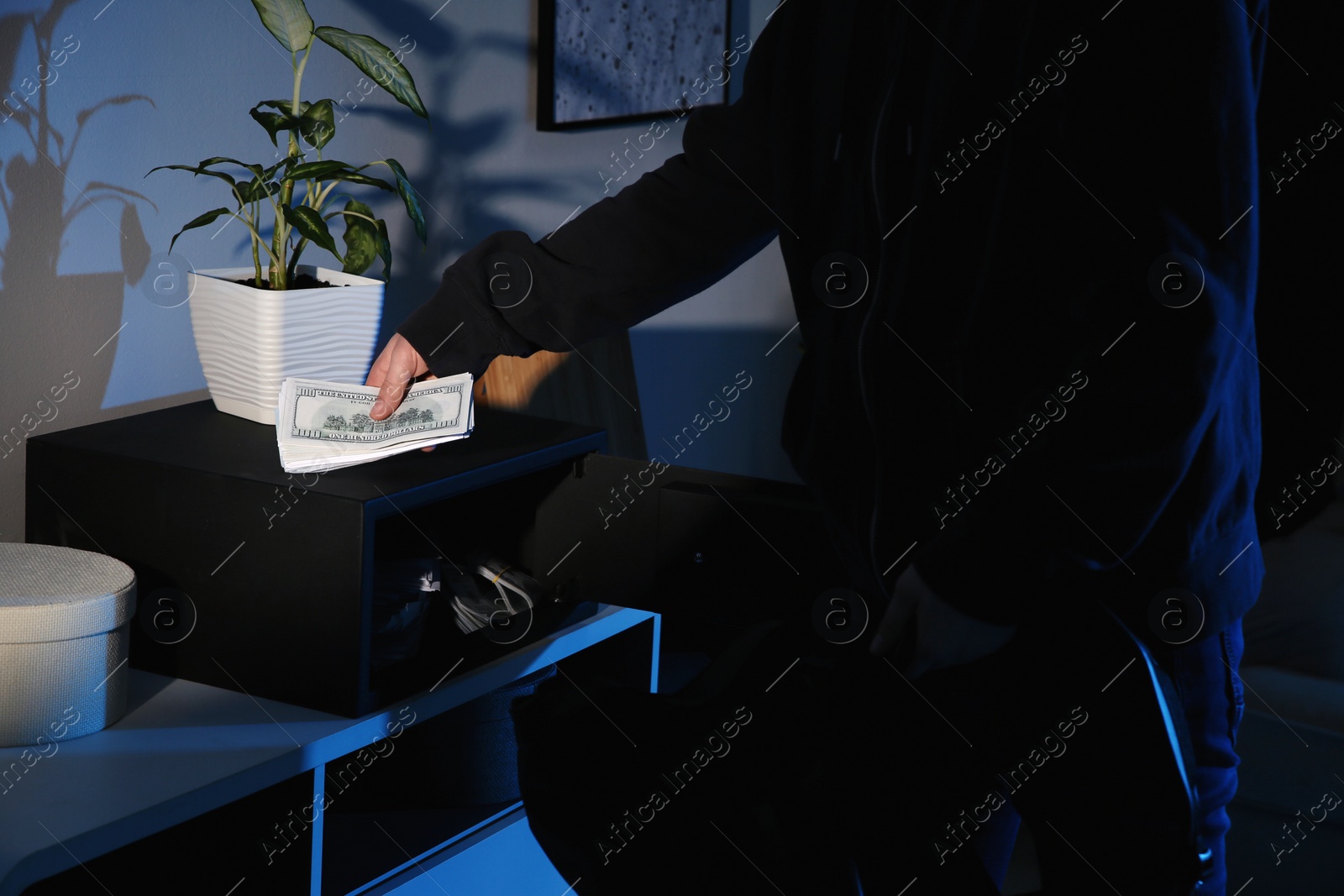 Photo of Thief taking money out of steel safe indoors at night, closeup