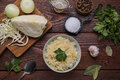 Photo of Bowl of tasty sauerkraut and ingredients on wooden table, flat lay