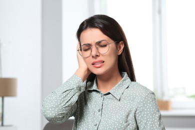 Photo of Young woman in eyeglasses suffering from ear pain indoors