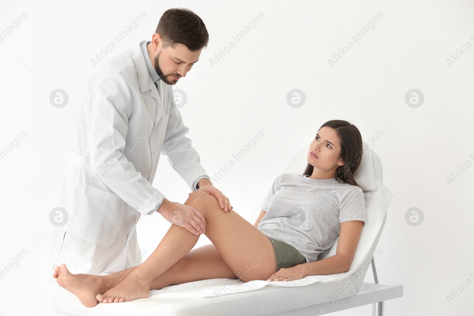 Photo of Doctor examining female patient with injured leg in clinic