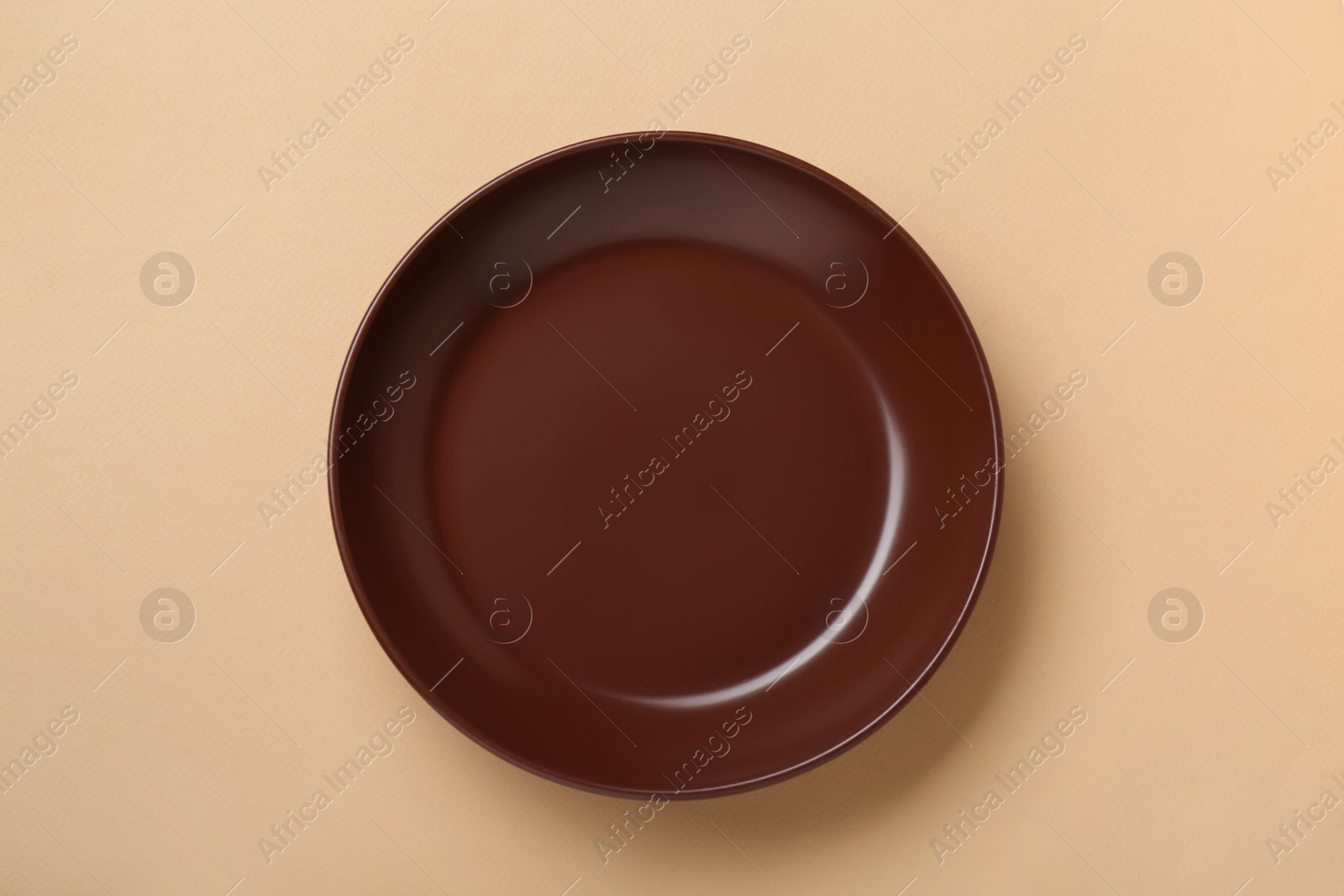 Photo of Empty brown ceramic plate on pale orange background, top view