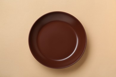 Empty brown ceramic plate on pale orange background, top view