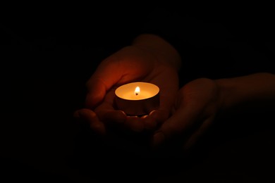 Photo of Woman holding burning candle in hands on black background, closeup