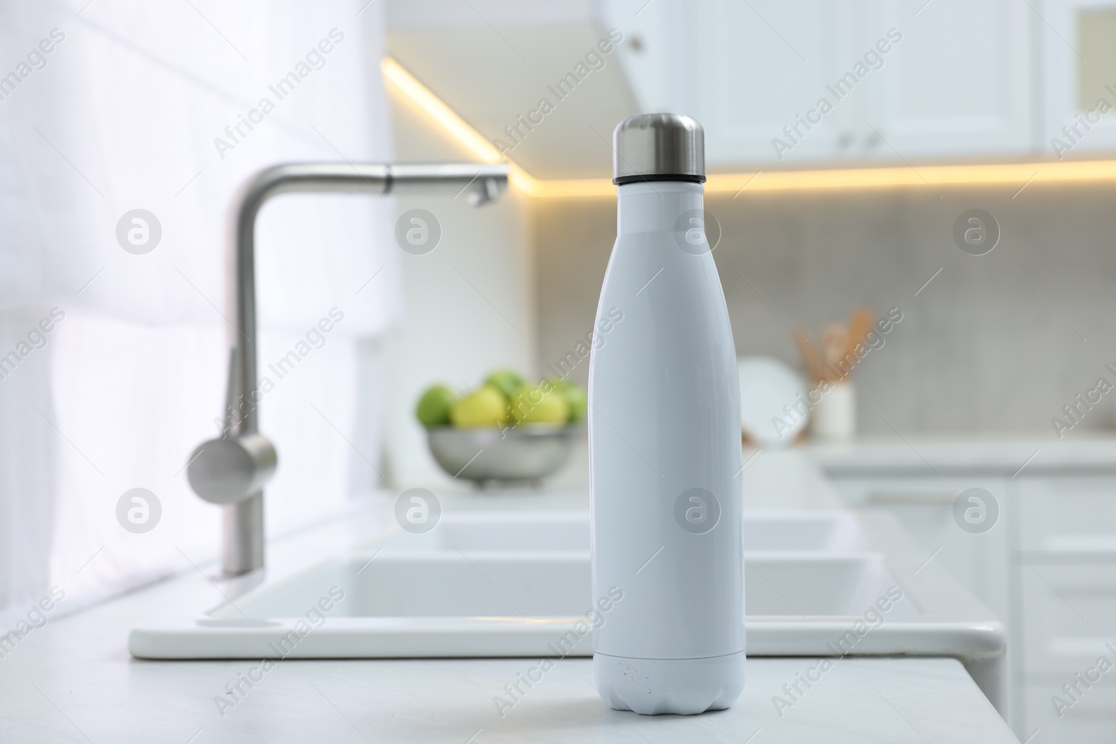 Photo of Stylish thermo bottle on white countertop in kitchen. Space for text