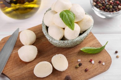 Photo of Tasty mozzarella balls, basil leaves and spices on white wooden table, closeup