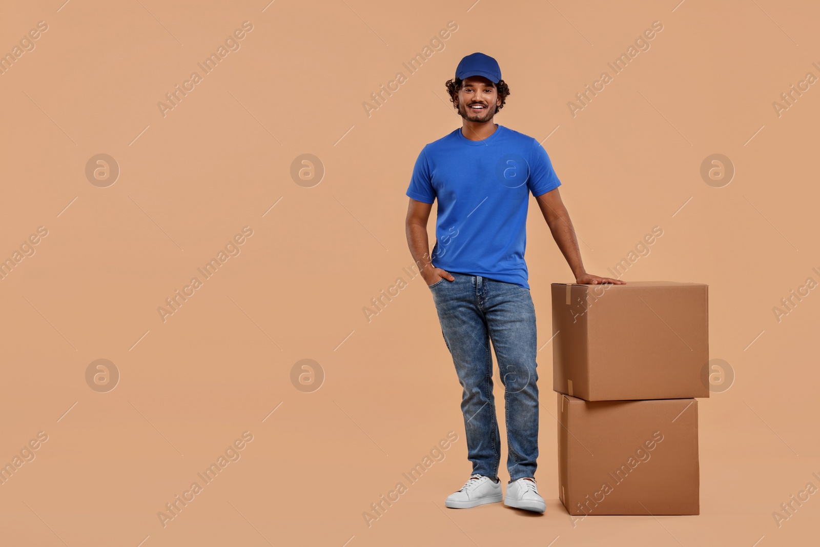 Photo of Happy courier with parcels on light brown background, space for text