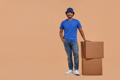 Photo of Happy courier with parcels on light brown background, space for text