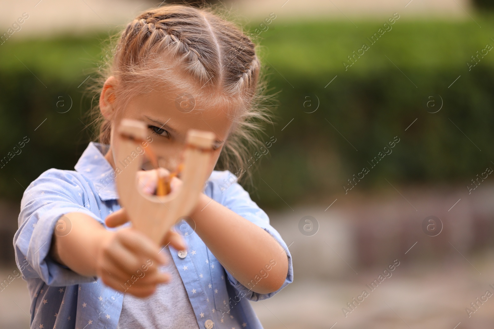 Photo of Little girl playing with slingshot outdoors. Space for text