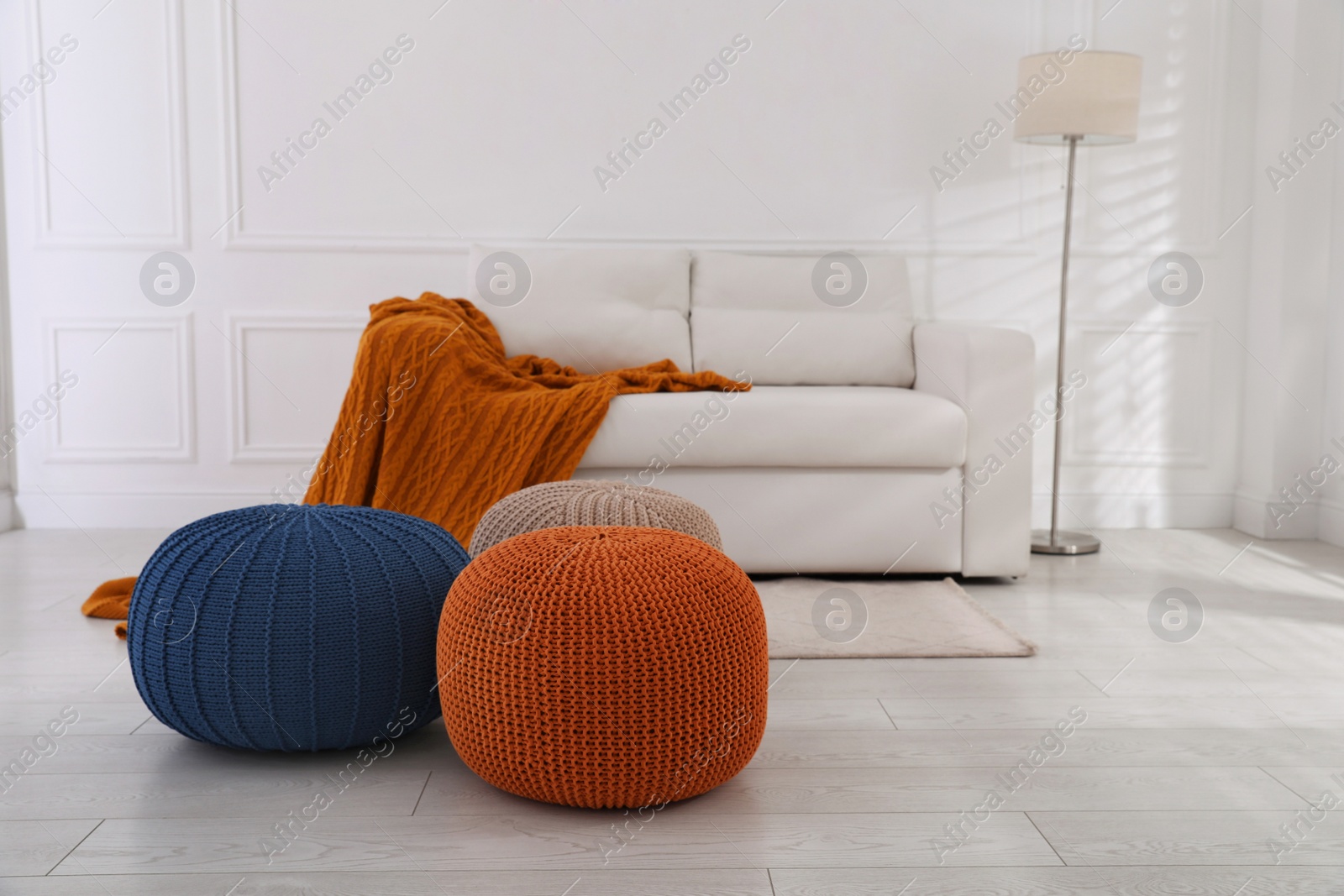 Photo of Stylish living room interior with white sofa and knitted poufs