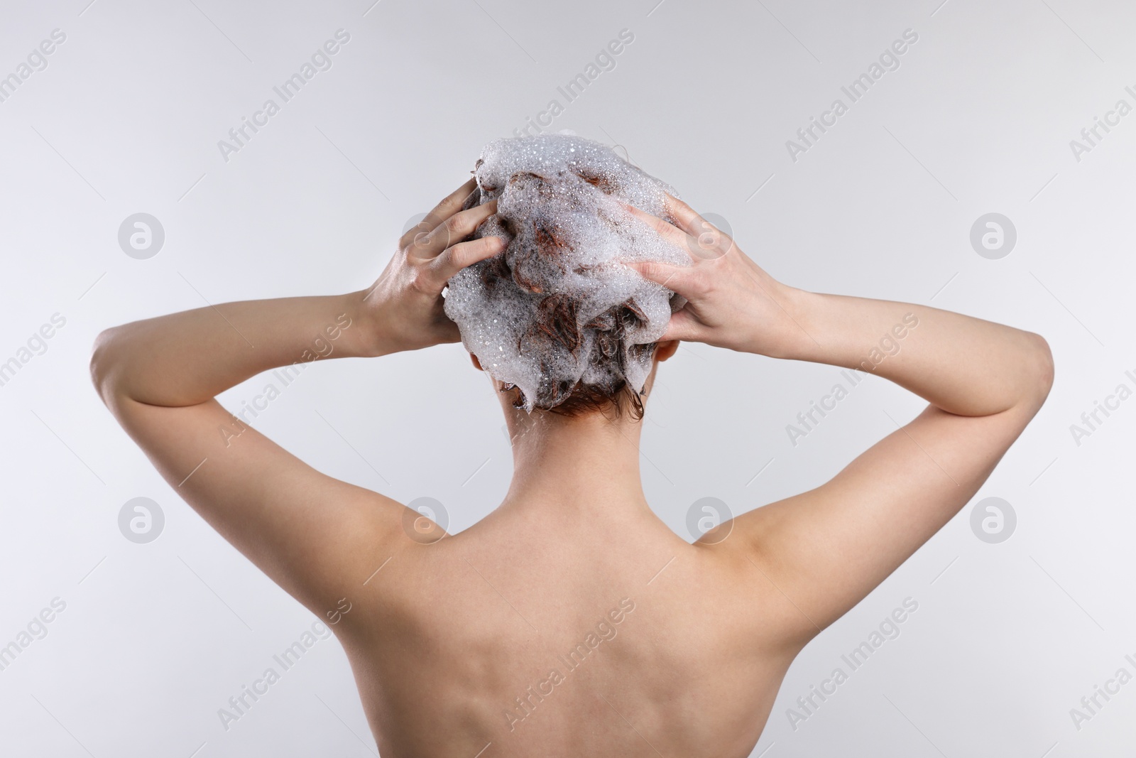 Photo of Young woman washing her hair with shampoo on light grey background, back view