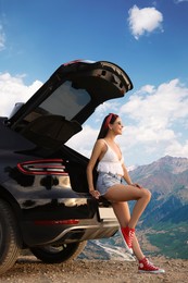 Image of Happy woman sitting in trunk of modern car in mountains
