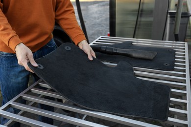 Photo of Man with auto carpets near vacuum cleaner at self-service car wash, closeup