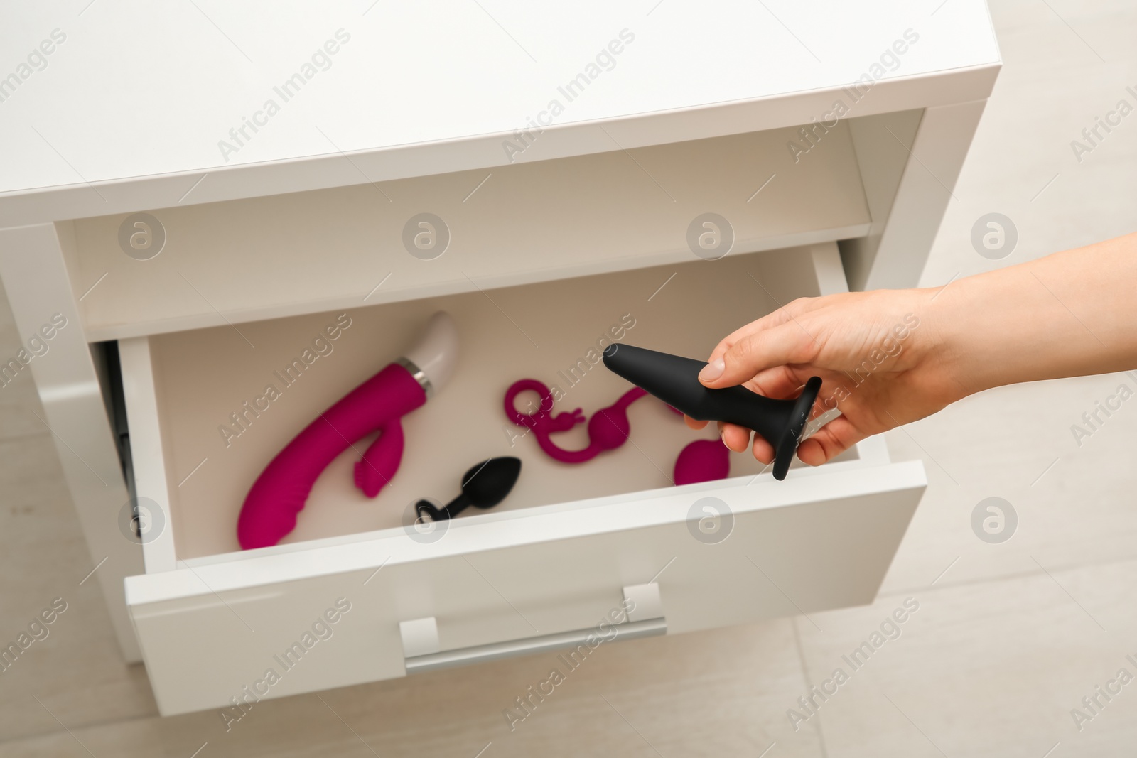 Photo of Woman taking anal plug from bedside table with other sex toys in room, closeup