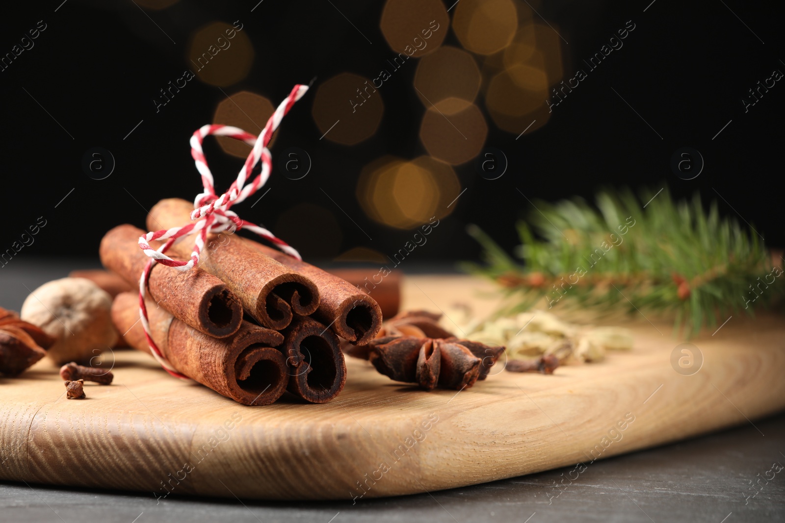 Photo of Cinnamon sticks and other spices on table against black background with blurred lights, closeup