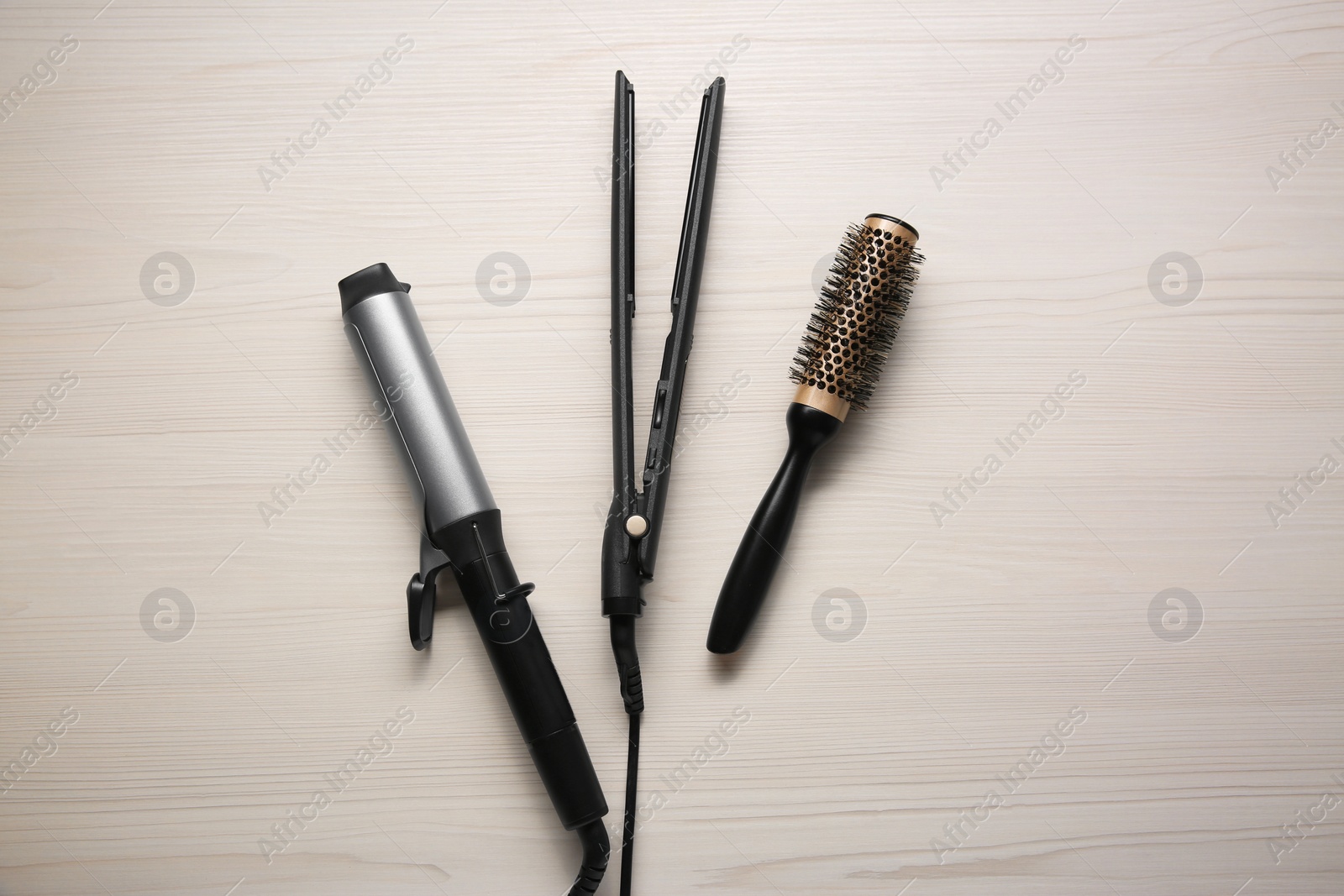 Photo of Curling iron, hair straightener and round brush on white wooden background, flat lay