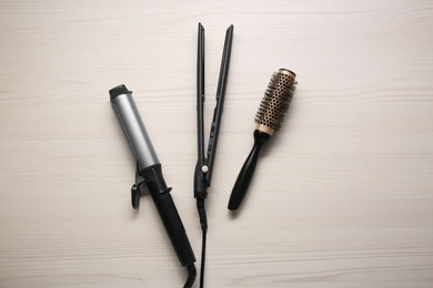 Photo of Curling iron, hair straightener and round brush on white wooden background, flat lay