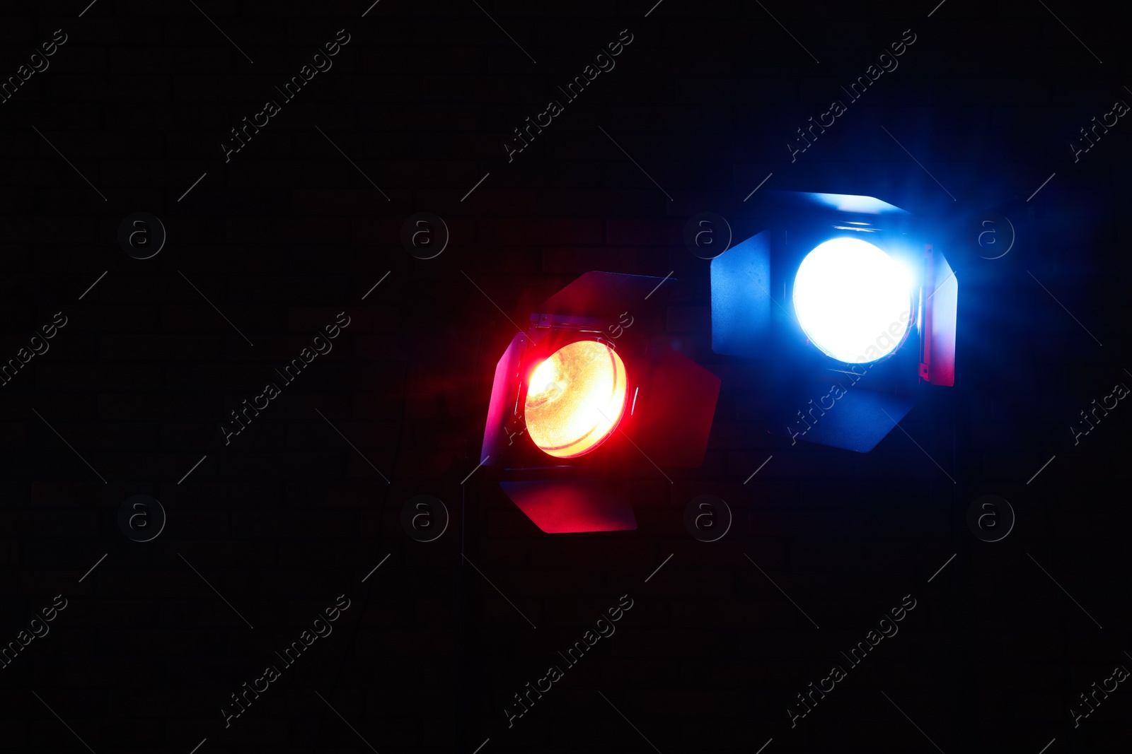 Photo of Bright blue and red spotlights near brick wall in dark room, space for text