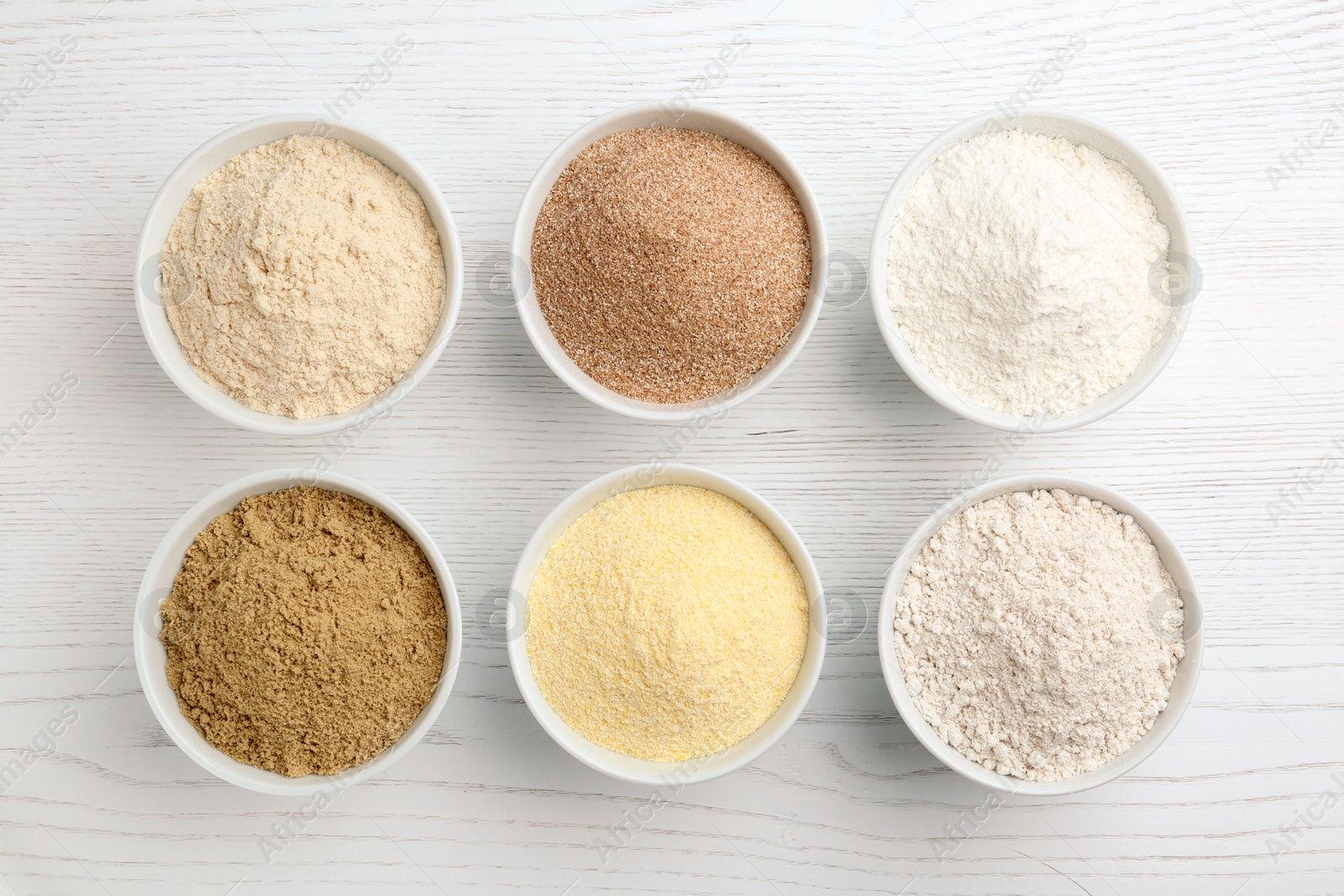 Photo of Bowls with different types of flour on white wooden background, top view