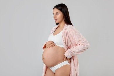 Beautiful pregnant woman in stylish comfortable underwear and robe on grey background