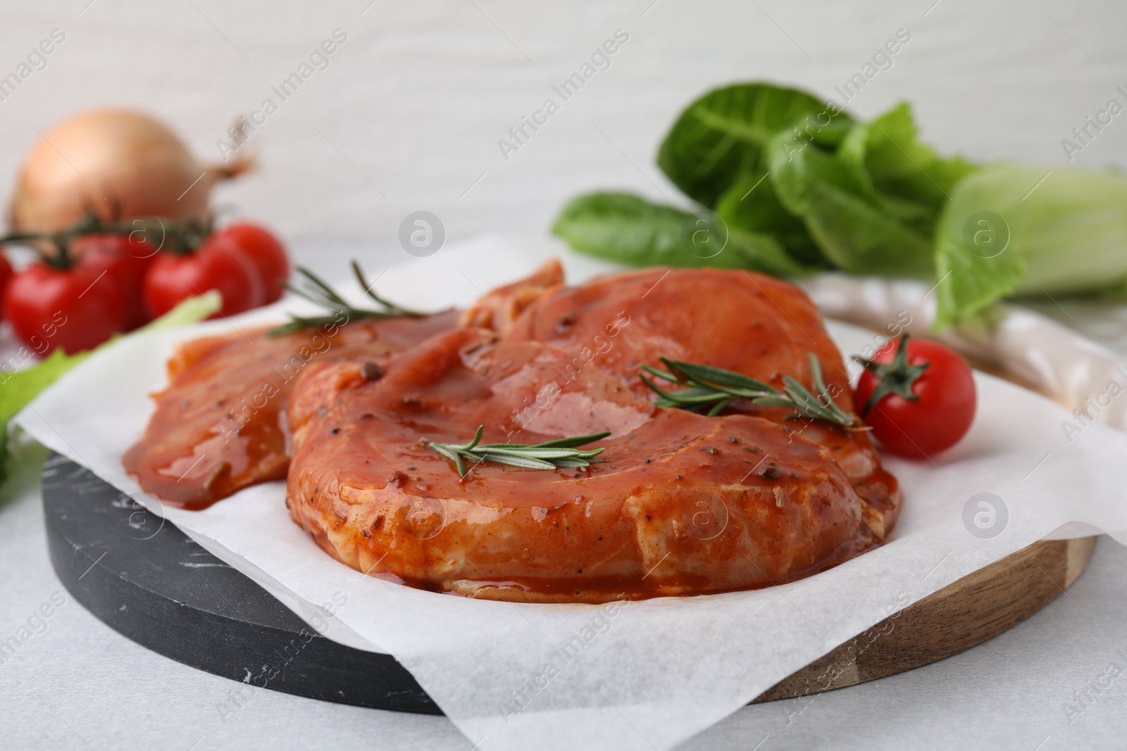 Photo of Board with raw marinated meat and rosemary on light table, closeup