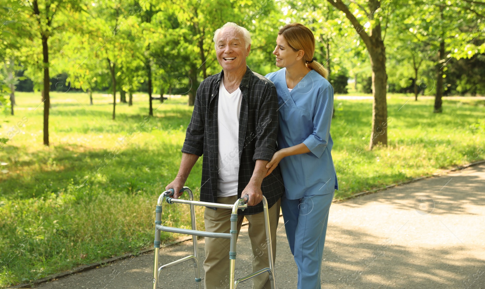 Photo of Happy nurse assisting elderly man with walking frame at park