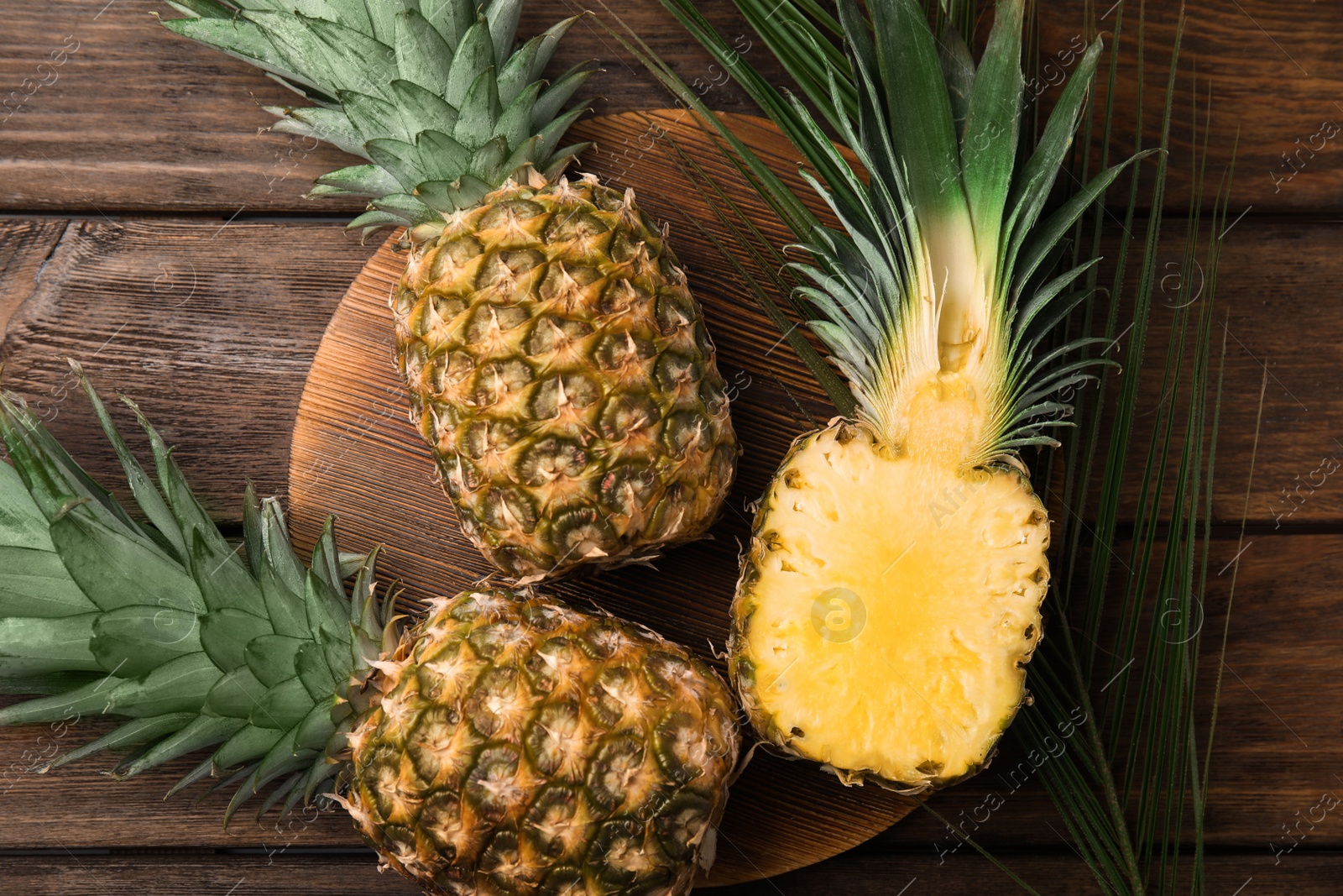 Photo of Whole and cut pineapples on wooden table, flat lay